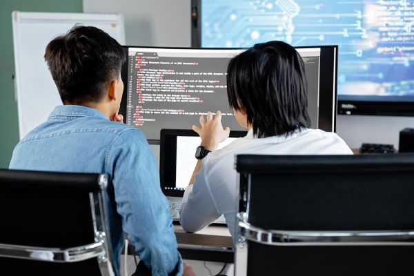 two people sitting in front of a comuter monitor.